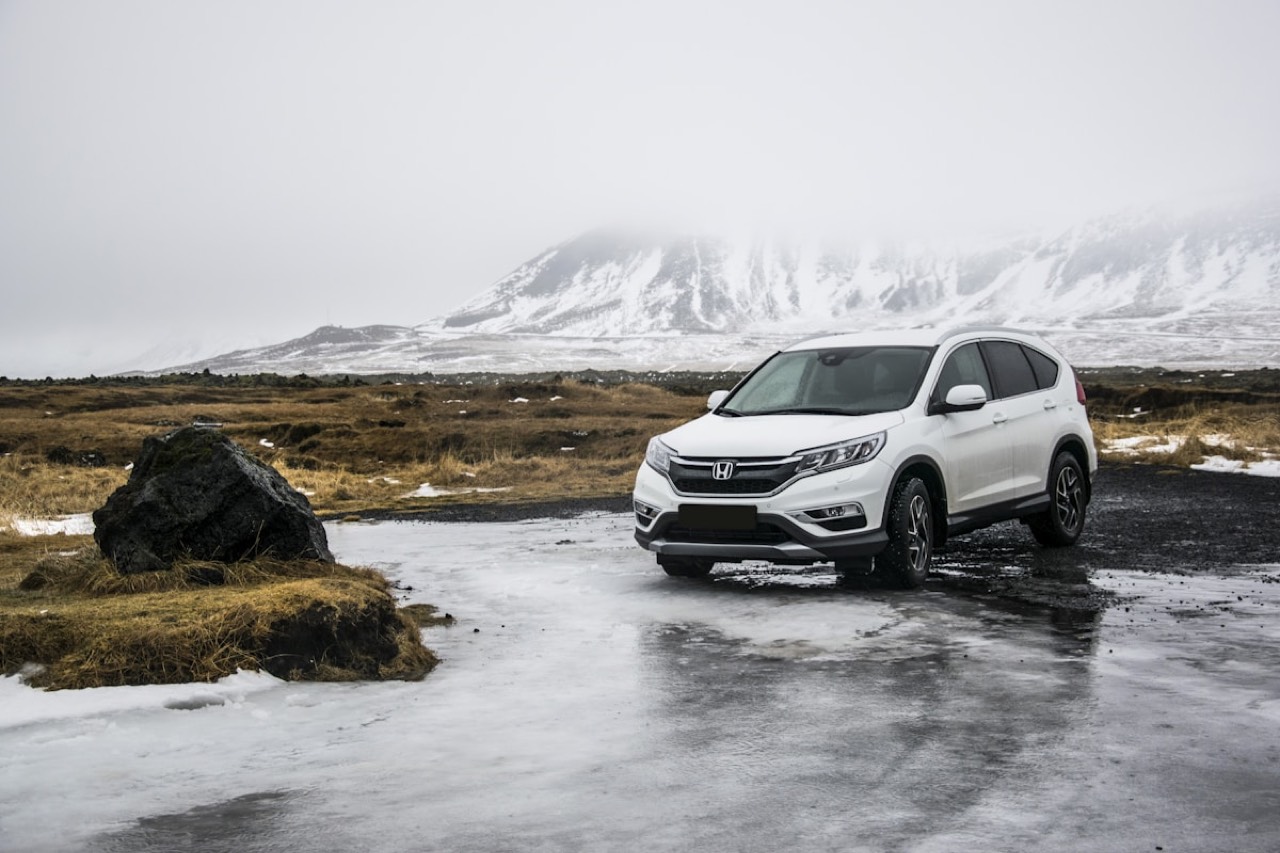 White Honda SUV parked on an icy road below snowy peaks