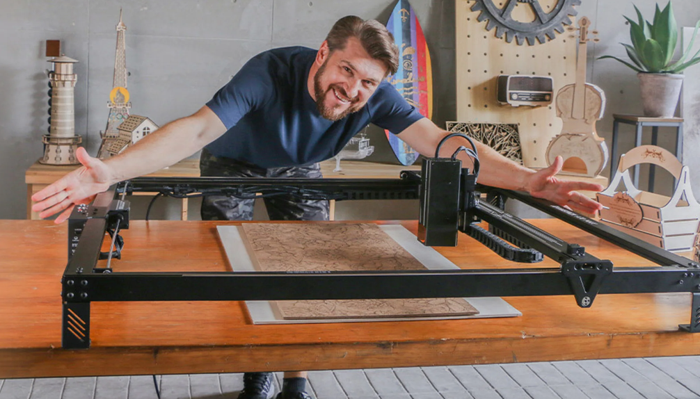 Maker leaning over an open-frame AtomStack diode engraver on a wooden bench with a large engraved leather panel finished on the bed