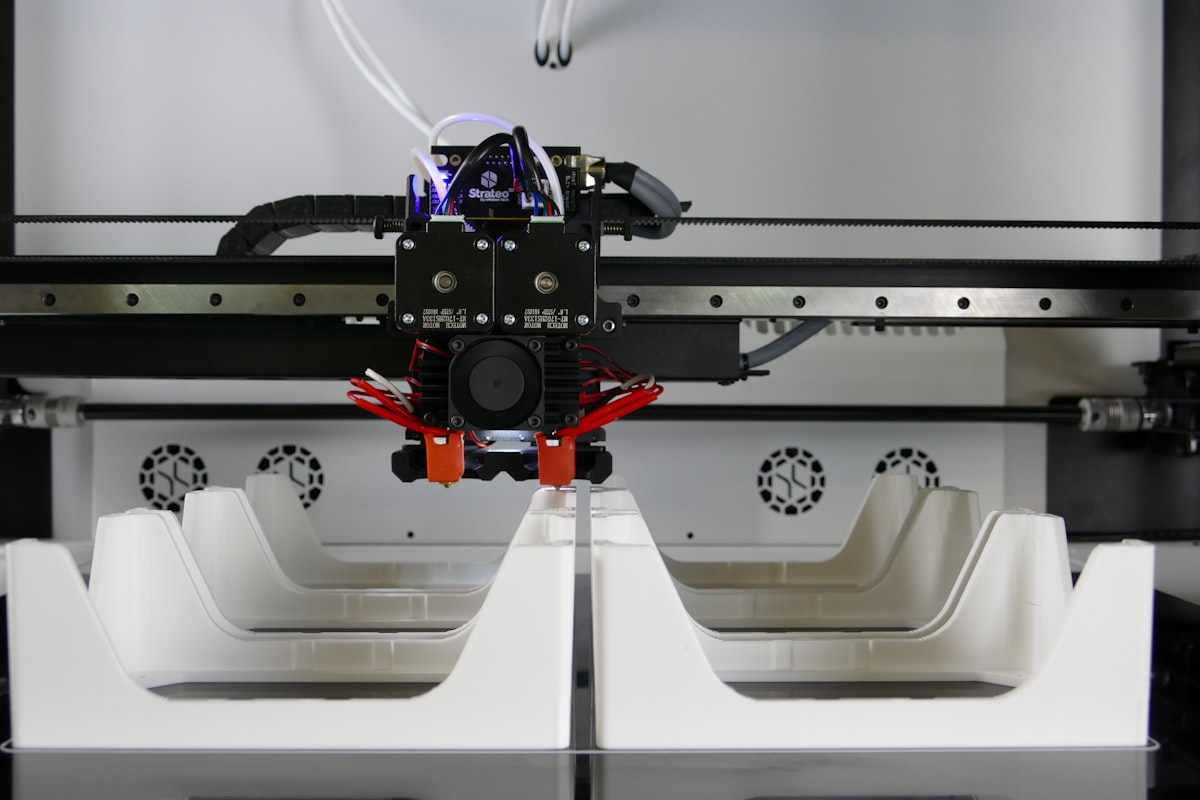 A 3D printer nozzle mid-print on a lattice-structured white part