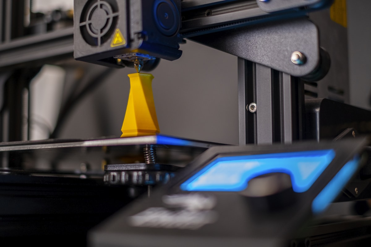 A 3D printer nozzle depositing orange filament onto a small printed part