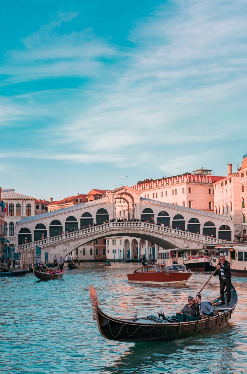 Arched stone bridge over a Venice canal with boats passing beneath