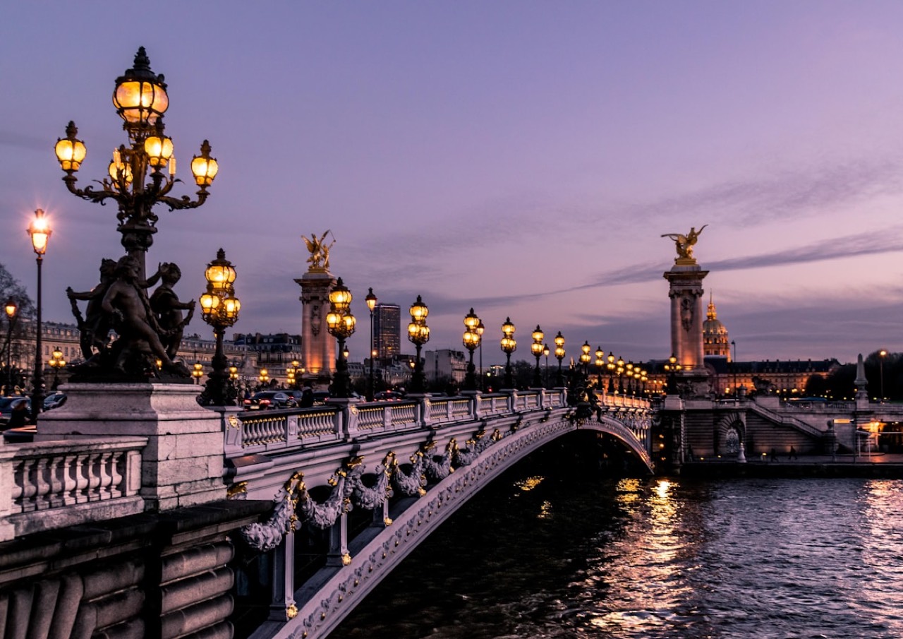 Illuminated Pont Alexandre III over the Seine at dusk with Paris skyline