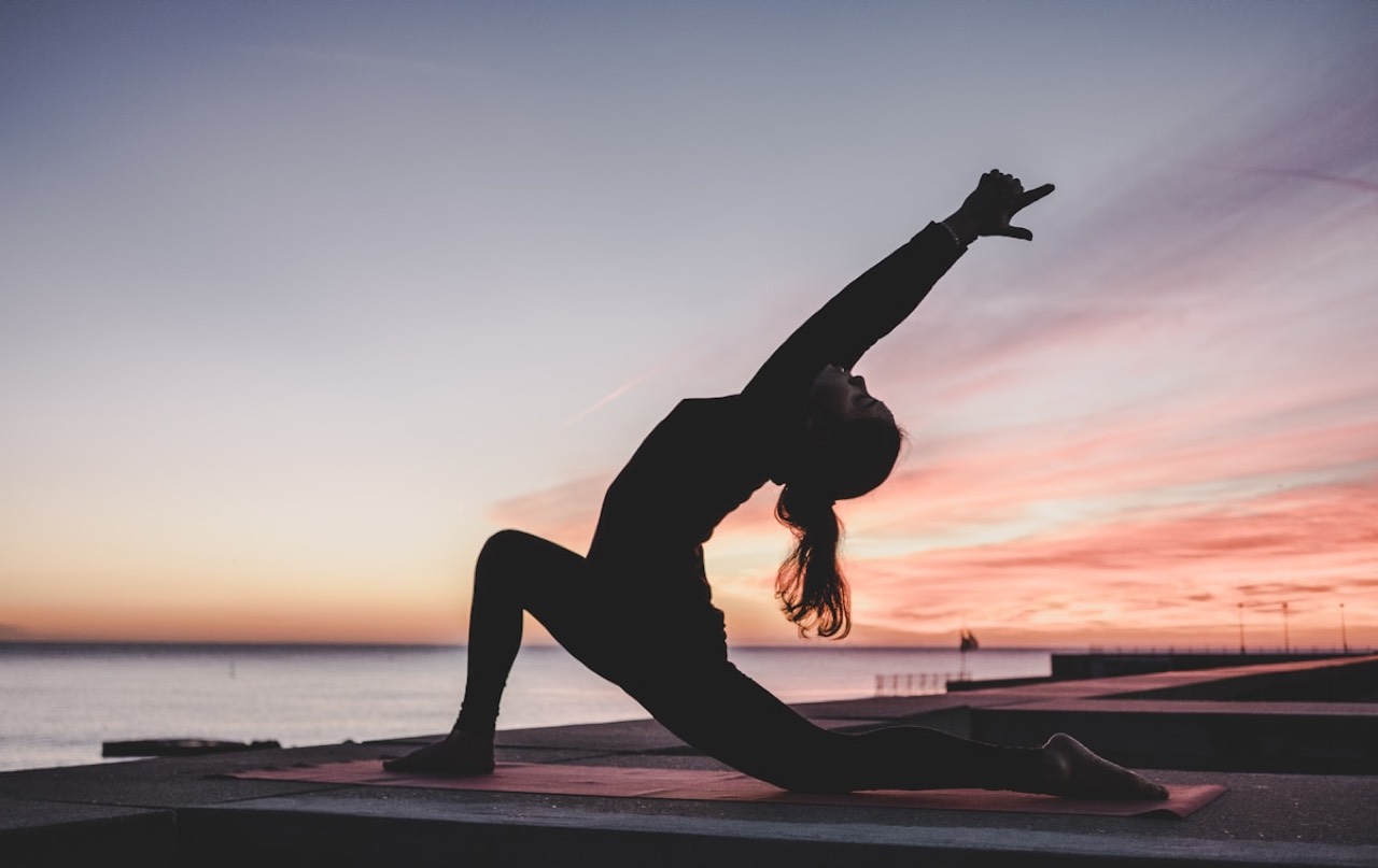 Silhouette of a woman in a sunset yoga pose by the sea
