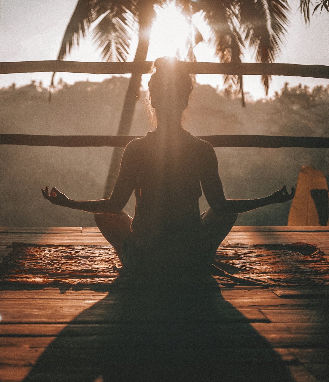 Person meditating cross-legged on a deck at sunrise