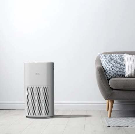 Levoit floor-standing air purifier beside a grey sofa in a bright living room