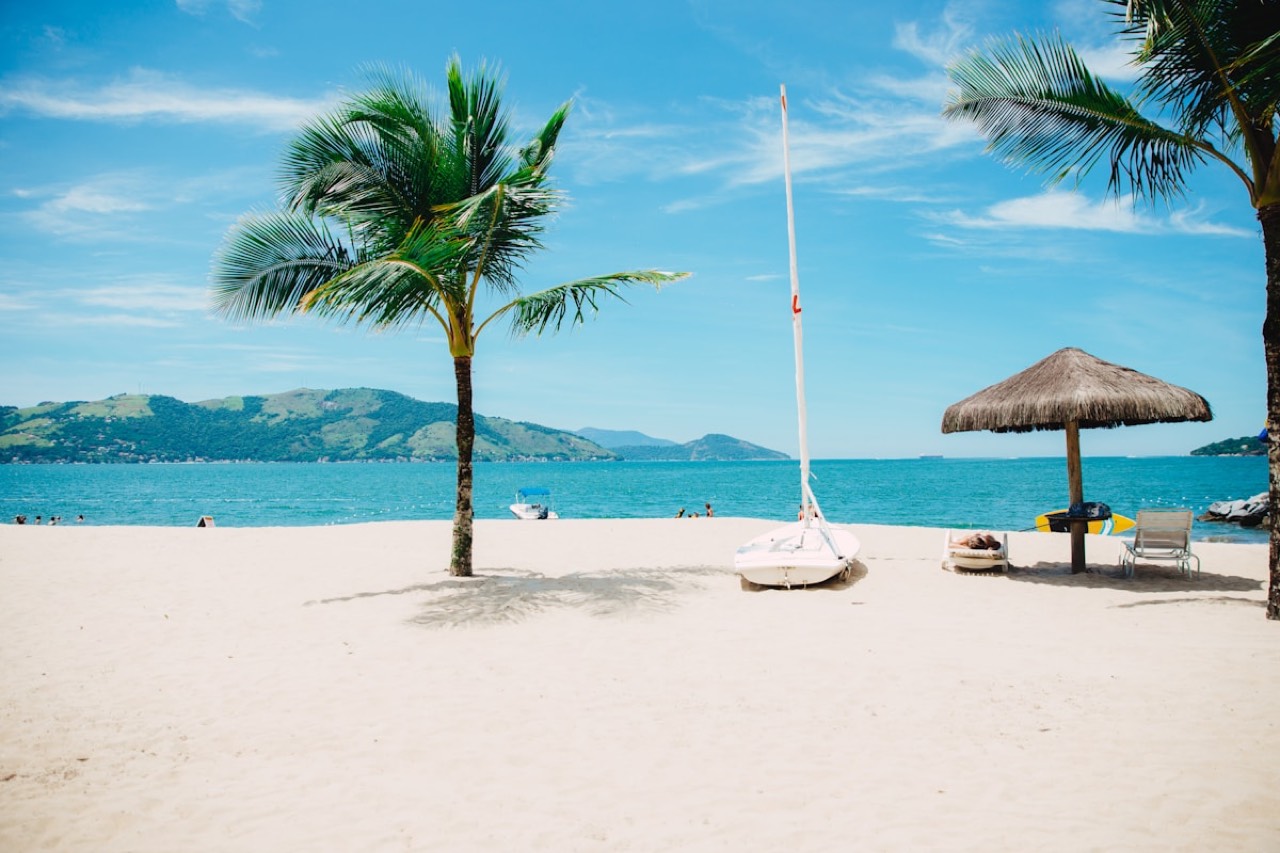 Palm-lined tropical beach with parasols, loungers and a sailboat offshore