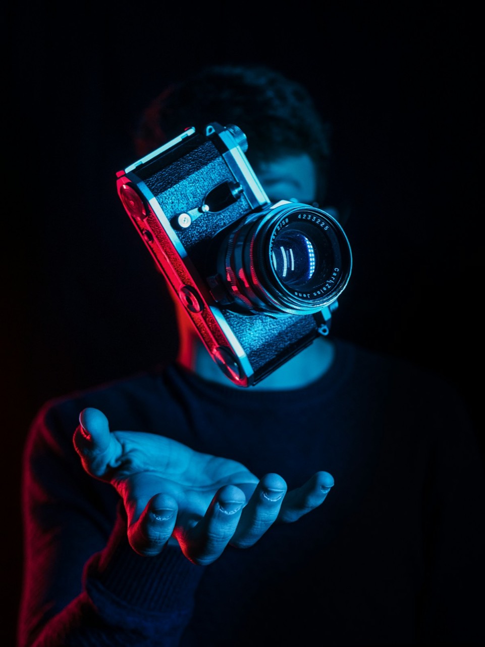 Person holding a silver retro-style camera up to their face against a dark background