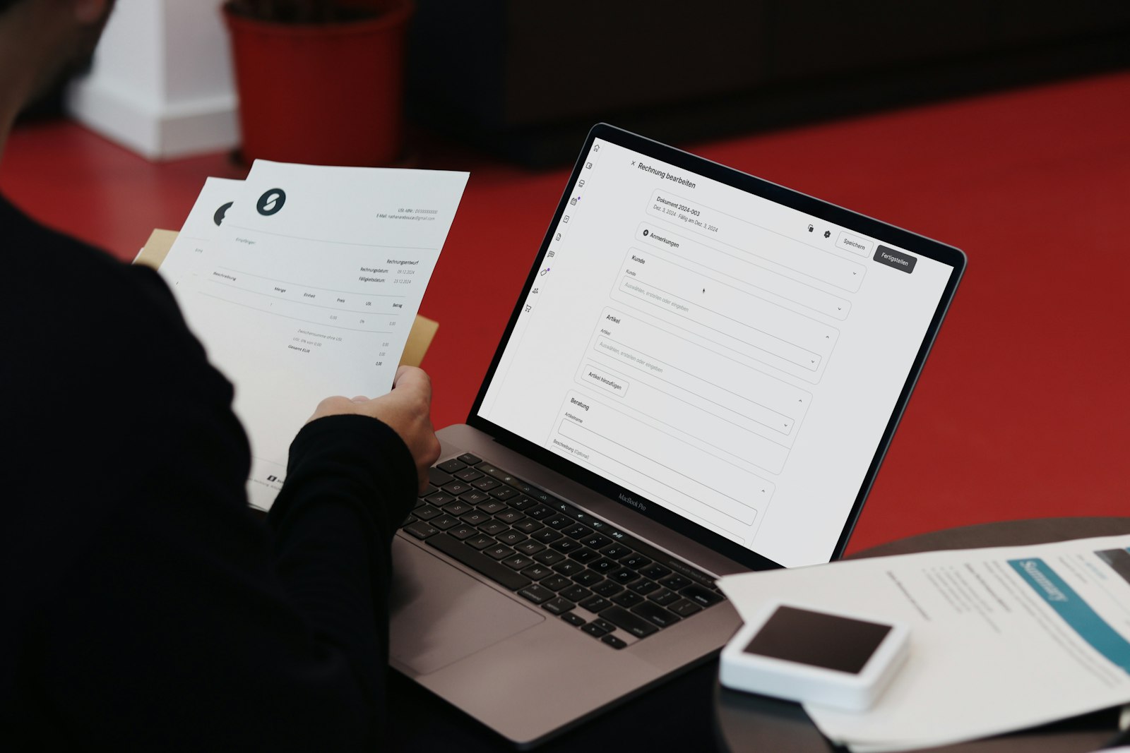 Person managing invoices on a laptop alongside paper documents