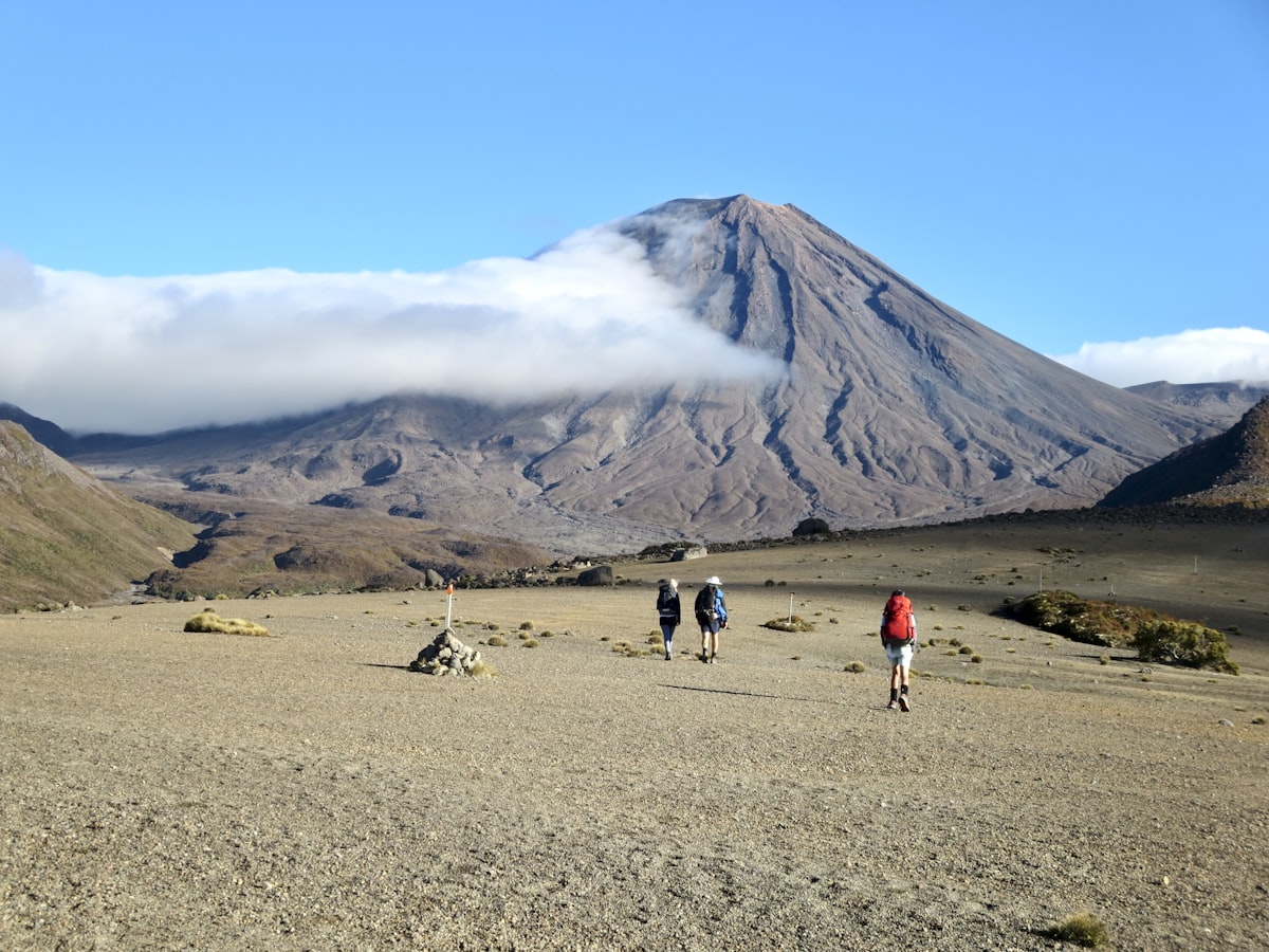 Three hikers on a mountain trail under a blue and white sky