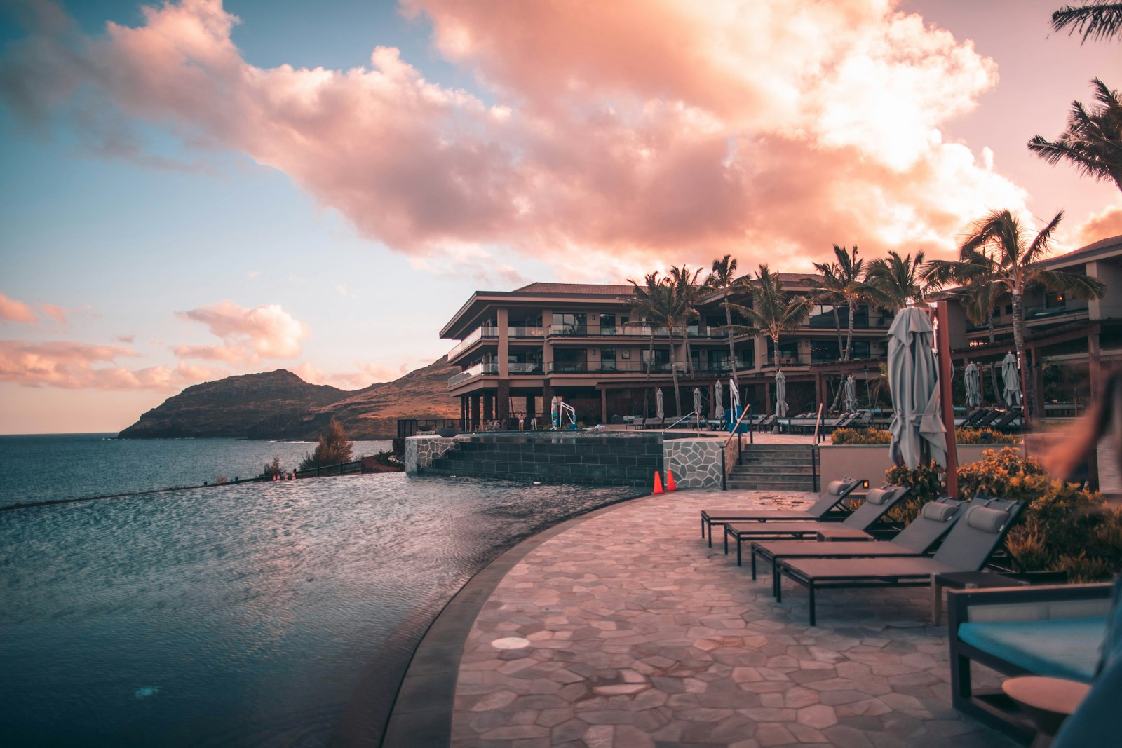 Infinity pool overlooking the ocean with palm trees and loungers at sunset